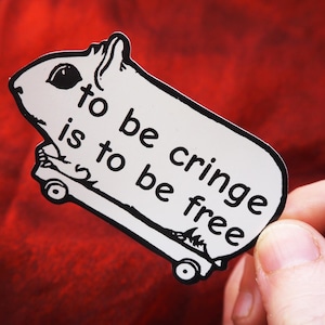 May include: A white sticker with a black outline featuring a cartoon guinea pig riding a skateboard. The sticker has the text "to be cringe is to be free" in black, bold font.