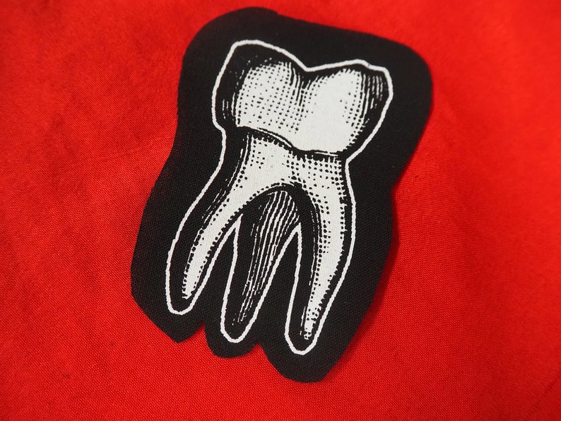 Pu&ograve; includere: Una toppa ricamata in bianco e nero di un dente su uno sfondo rosso.