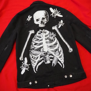 Puede incluir: Chaqueta vaquera negra con un esqueleto blanco e insectos impresos en la espalda.