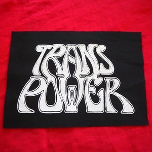 Op de afbeelding: Zwarte patch met witte tekst die "TRANS POWER" in een gestileerd lettertype leest.
