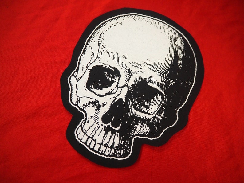 May include: Black and white skull patch with a detailed illustration of a human skull. The skull is outlined in black and has a white background.