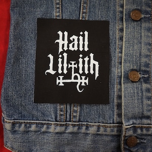 Peut inclure: Veste en jean noire avec un patch noir sur lequel est inscrit "Hail Lilith" en lettres gothiques blanches.