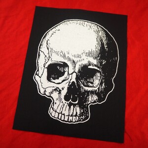 May include: A black and white iron-on patch featuring a detailed skull graphic. The skull is white with black eye sockets and teeth.