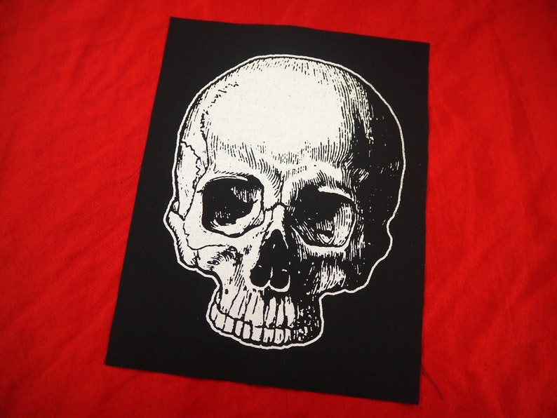 May include: A black and white iron-on patch featuring a detailed skull graphic. The skull is white with black eye sockets and teeth.