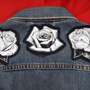 May include: Three black and white iron-on patches of roses on a blue denim jacket.