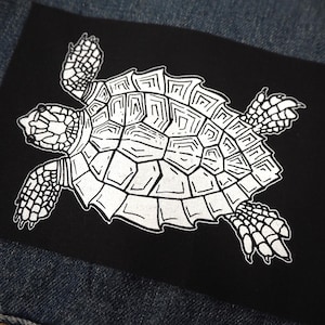 Peut inclure: Un patch noir avec un contour blanc d'une tortue avec un motif de carapace détaillé.