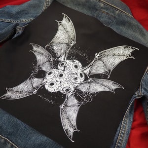 Op de afbeelding: Zwart-witte illustratie van een vleermuis met meerdere ogen op een zwarte achtergrond. De vleermuis heeft vier vleugels en is omringd door een sterrenhemel.