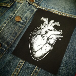 May include: A black denim jacket with a white anatomical heart patch sewn on the front. The patch is on a black background.