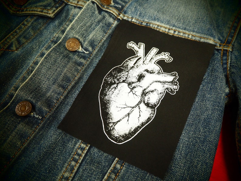 May include: A black denim jacket with a white anatomical heart patch sewn on the front. The patch is on a black background.