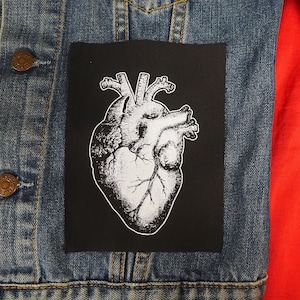 Peut inclure: Un patch représentant une illustration anatomique d'un cœur en noir et blanc sur une veste en jean. Le patch est cousu sur la veste.