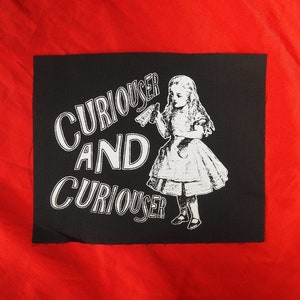 Puede incluir: Parche de tela negro con texto blanco y una imagen blanca de Alicia de Alicia en el País de las Maravillas. El texto dice "Curiouser and Curiouser".