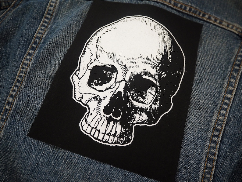 May include: A black and white skull patch with a detailed illustration of a human skull. The skull is facing to the right and has a white outline.