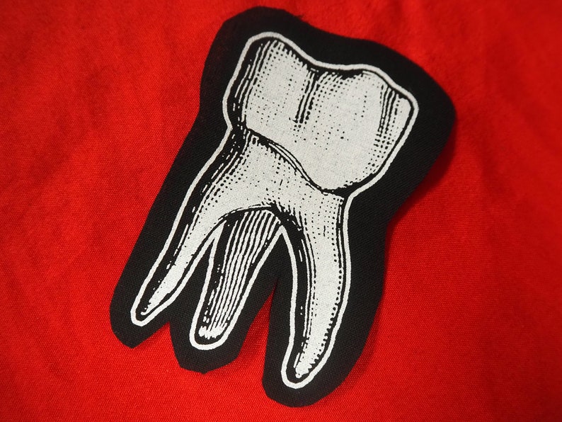 Pu&ograve; includere: Una toppa termoadesiva in bianco e nero a forma di dente. Il dente &egrave; un'illustrazione dettagliata di un molare con contorno bianco e ombreggiatura nera.