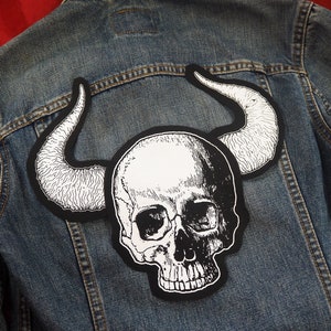 May include: A black and white skull with horns patch, perfect for adding a rebellious touch to a denim jacket.