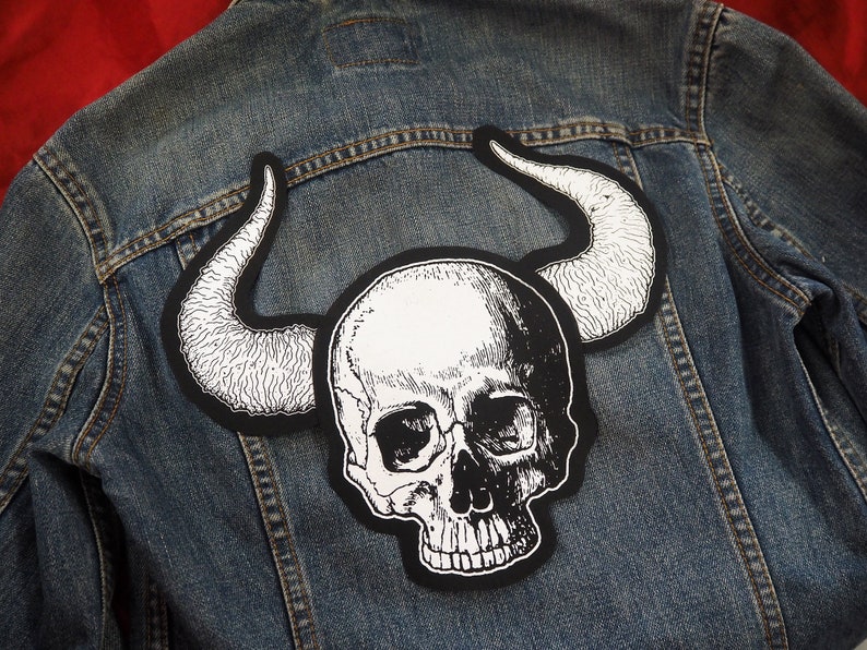 May include: A black and white skull with horns patch, perfect for adding a rebellious touch to a denim jacket.