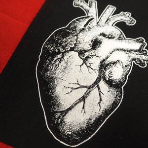May include: A black and white anatomical heart illustration printed on a black fabric patch. The heart is detailed with veins and arteries.