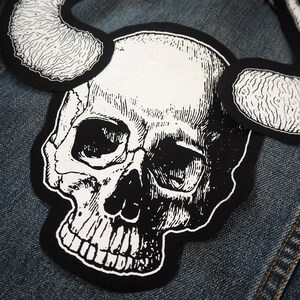 May include: A black and white skull with horns, sewn onto a denim jacket.