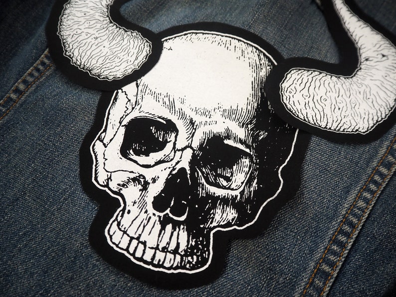 May include: A black and white skull with horns, sewn onto a denim jacket.