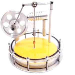 Puede incluir: Un modelo en miniatura de motor de vapor plateado con una base amarilla. El modelo presenta un volante, un pistón y varios componentes mecánicos. El motor está encerrado en una carcasa circular transparente.