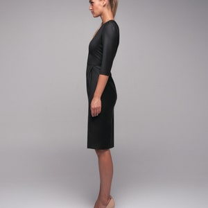 May include: A woman wearing a black knee-length dress with a fitted silhouette and three-quarter sleeves. She is wearing nude heels.