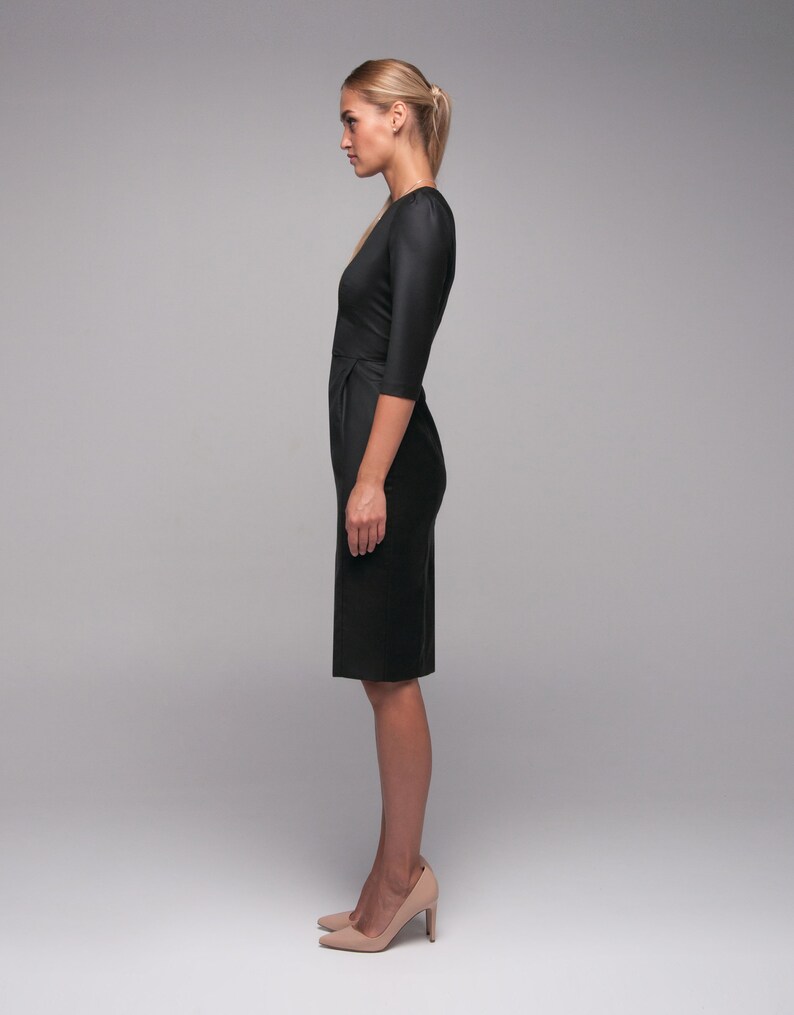 May include: A woman wearing a black knee-length dress with a fitted silhouette and three-quarter sleeves. She is wearing nude heels.