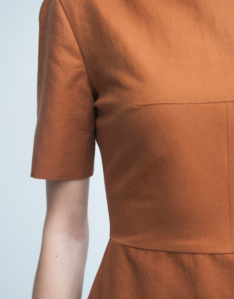 May include: A rust-colored short-sleeved dress with a simple, fitted silhouette.