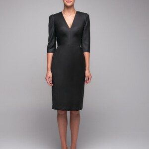 May include: A woman wearing a black knee-length dress with a V-neckline and three-quarter sleeves. She is wearing nude heels.