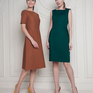 May include: Two women wearing dresses, one in brown and one in green, stand in front of a white wall with decorative molding. Both women are wearing high heels.