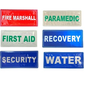 Könnte beinhalten: Sechs rechteckige reflektierende Sicherheitszeichen mit weißem Text auf farbigem Hintergrund. Die Schilder zeigen "Fire Marshall", "Paramedic", "First Aid", "Recovery", "Security" und "Water".