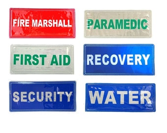 Puede incluir: Seis señales de seguridad reflectantes rectangulares con texto blanco sobre un fondo de color. Las señales dicen "Fire Marshall", "Paramedic", "First Aid", "Recovery", "Security" y "Water".