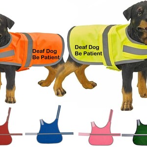 May include: Two Rottweiler dogs wearing high-visibility vests. One vest is orange, the other is yellow. Both vests have reflective stripes and the text "Deaf Dog Be Patient". Below are vests in red, blue, pink, and green.
