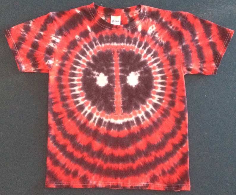 May include: Red, black, and white tie-dye t-shirt with a black and white Deadpool mask design in the center.