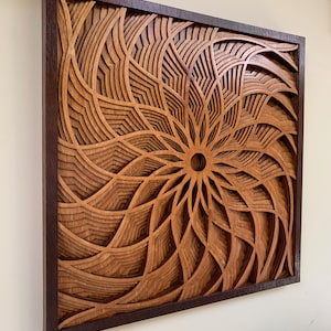 May include: A wooden wall art piece with a geometric design in shades of brown. The design is a spiral pattern with a central hole. The piece is framed in a dark brown wood frame.