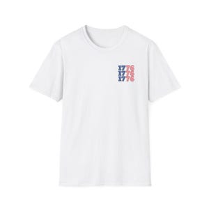 May include: White t-shirt with a red, white and blue American flag design and the number 1776 repeated three times.