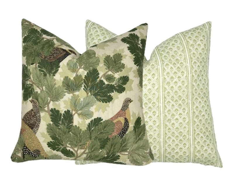 May include: Two decorative throw pillows with a nature theme. One pillow features a green and brown bird and leaf pattern on a cream background. The other pillow has a green and white geometric pattern.