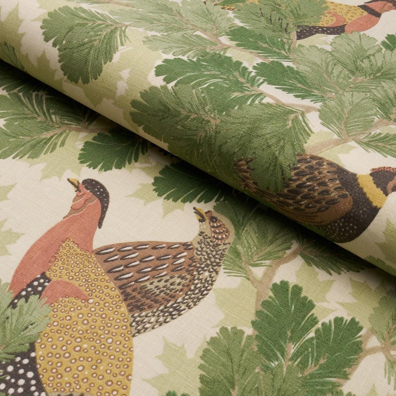 May include: A beige fabric with a repeating pattern of green pine branches and colorful birds. The birds are brown, red, and yellow with black markings.