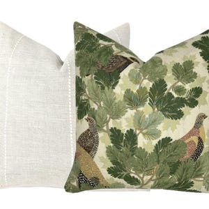 May include: Two decorative throw pillows, one with a white linen fabric and the other with a green and brown patterned fabric featuring birds and leaves.