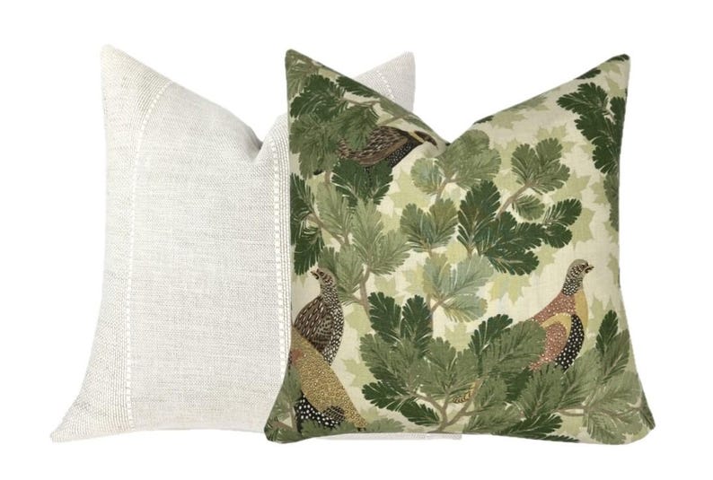 May include: Two decorative throw pillows, one with a white linen fabric and the other with a green and brown patterned fabric featuring birds and leaves.