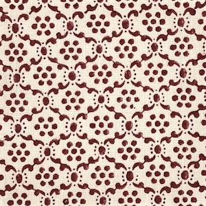 May include: A woven fabric featuring a repeating pattern of dark maroon floral motifs printed on a cream-colored background. The design consists of small circular clusters of dots arranged in a grid, connected by curved, symmetrical vine-like shapes.