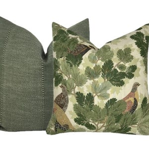 May include: Two decorative throw pillows. One pillow is green with a subtle textured pattern. The other pillow is white with a green and brown pattern of leaves and birds.