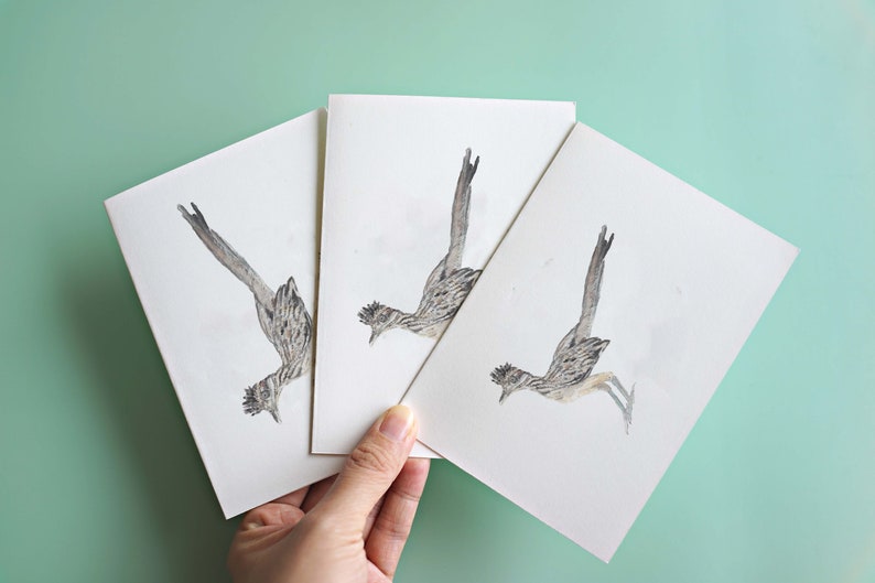 Peut inclure: Trois cartes blanches avec une illustration aquarelle d'un oiseau coureur des routes sur chaque carte. L'oiseau est repr&eacute;sent&eacute; en vol, les ailes d&eacute;ploy&eacute;es.
