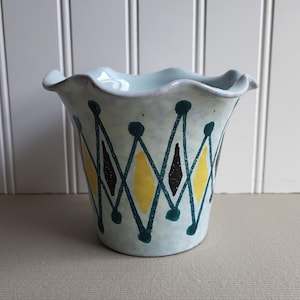 May include: A light blue ceramic planter with a scalloped rim and a geometric design in yellow, black, and teal.