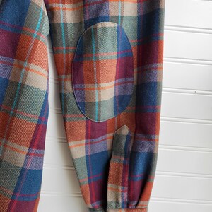 Peut inclure: Gros plan d'une chemise &agrave; carreaux &agrave; manches longues dans les tons bordeaux, bleu, orange et vert. Le coude est assorti. Le poignet a une fermeture &agrave; bouton.