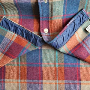 Peut inclure: Gros plan d'une chemise &agrave; carreaux dans les tons de bleu, orange, rouge et vert. La chemise a un col bleu et une petite &eacute;tiquette qui indique "nettoyage &agrave; sec uniquement". Le tissu est textur&eacute; et la chemise est boutonn&eacute;e.