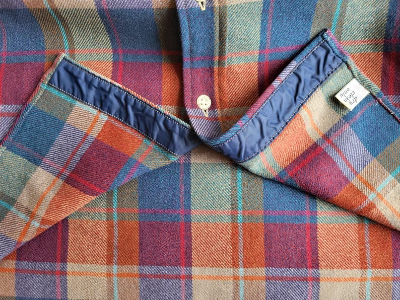 Peut inclure: Gros plan d'une chemise &agrave; carreaux dans les tons de bleu, orange, rouge et vert. La chemise a un col bleu et une petite &eacute;tiquette qui indique "nettoyage &agrave; sec uniquement". Le tissu est textur&eacute; et la chemise est boutonn&eacute;e.
