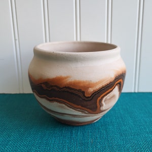 May include: A white ceramic pot with brown and orange marbling. The pot is round and has a wide opening.