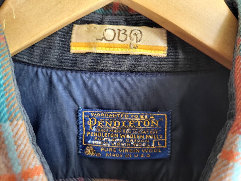 Peut inclure: Gros plan sur une chemise en laine Pendleton avec un col en velours c&ocirc;tel&eacute; bleu et une doublure bleue. La chemise pr&eacute;sente un motif &agrave; carreaux color&eacute; orange, sarcelle et rouge. L'&eacute;tiquette Pendleton est visible, avec le texte "Pure Virgin Wool Made in U.S.A."