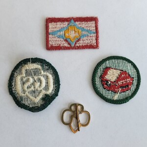 May include: Four embroidered patches, two green, one red, and one white, with a gold pin. The green patches have white embroidered designs, one with a flower and the other with a house. The red patch has a white embroidered design with a blue and white star. The white patch has a gold embroidered design with a blue and white star.