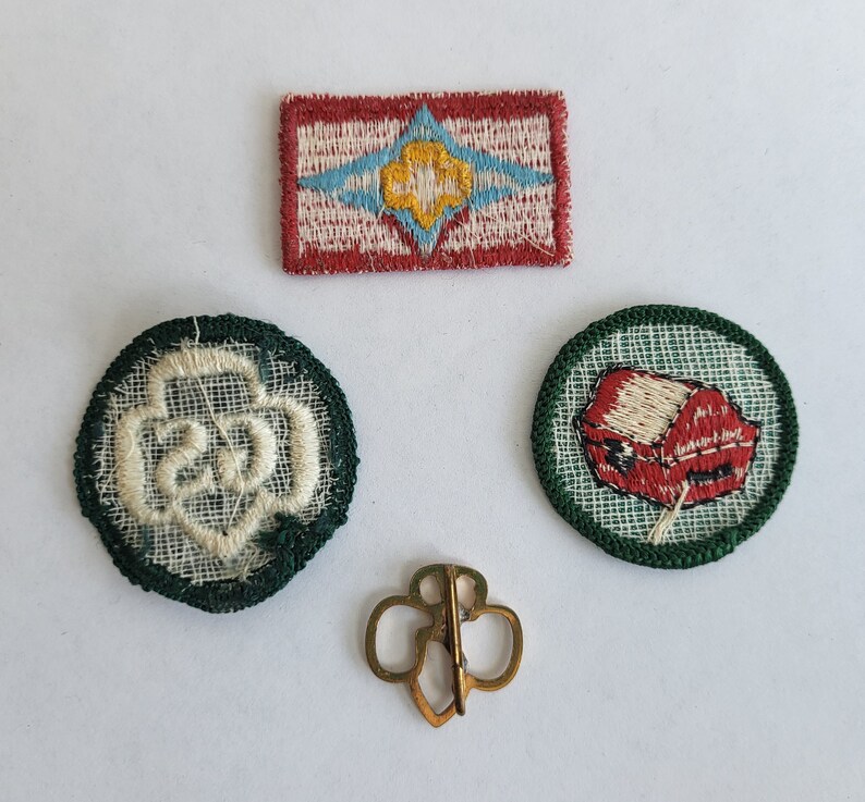 May include: Four embroidered patches, two green, one red, and one white, with a gold pin. The green patches have white embroidered designs, one with a flower and the other with a house. The red patch has a white embroidered design with a blue and white star. The white patch has a gold embroidered design with a blue and white star.
