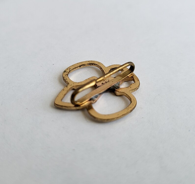 May include: Gold-toned metal clasp with a clover design. The clasp is open and ready to be attached to a garment.
